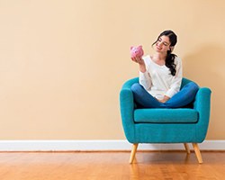Woman sitting on her couch and holding a piggy bank